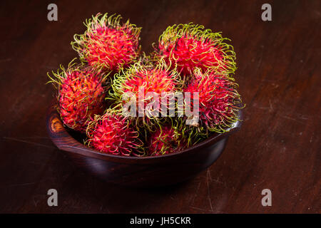 Holzschale gefüllt mit Rambutan platziert auf einem Holztisch, Rambutan ist eine süße, tropische Frucht. Stockfoto