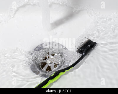 Zahnbürste liegen in der Spüle mit fließendem Wasser. Badezimmerthema Stockfoto