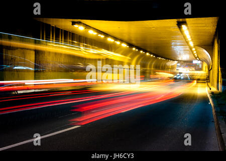 Nachtverkehr auf Straßen der Stadt. Fahrzeuge, die in und aus dem Tunnel in Bewegung verwischen Stockfoto