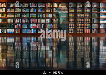 ein Waman war Passong viele Bücherregale mit einer Reflexion auf dem Boden in einer Bibliothek Stockfoto