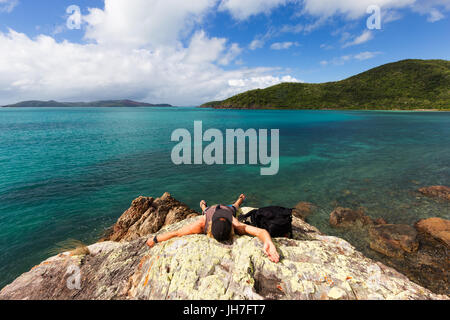 Eine erschöpfte Reisende ruht auf einem Felsen an einem schönen abgelegenen tropischen Strand in Nord-Queensland, Australien. Stockfoto