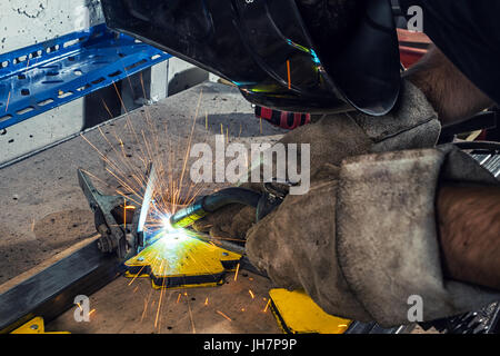 Close-up ein junger Mann Schweißer trägt einen schwarzen Schweißen Maske und Gebäude Häkelt ist ein Metall schweißen Schweißgerät in einem Workshop Stockfoto