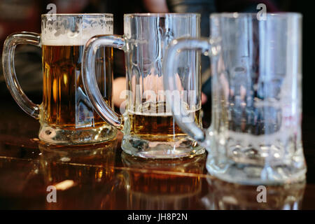 Drei Kannen mit einer unterschiedlichen Menge Bier in Ihnen Stockfoto