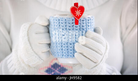 Gestrickter Wolle-Cup in Menschenhand. Mit roten Herzen. Stockfoto