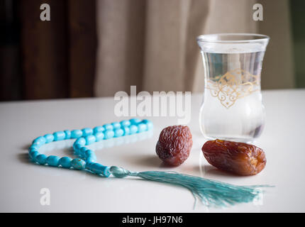 Zwei frische Datteln Medjool, Glas Wasser und Rosenkranz auf weißen Tisch. Stockfoto