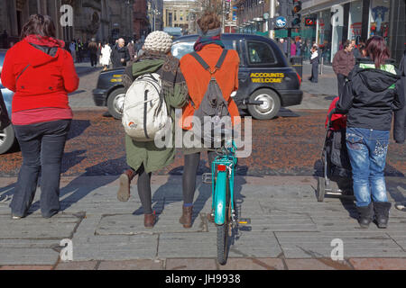 Buchanan Street Fußgänger warten am Bordstein junge Mädchen Radfahrer mit Rucksäcken auf Gehweg Bürgersteig Stockfoto