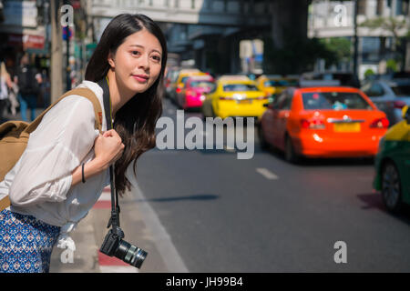 Frau wartenden Taxi auf der Straße. Asiatin mit rufen ein Taxi auf der Straße, Bangkok Thailand. Reisende, die mit Telefon app Technologie für Pkw Stockfoto