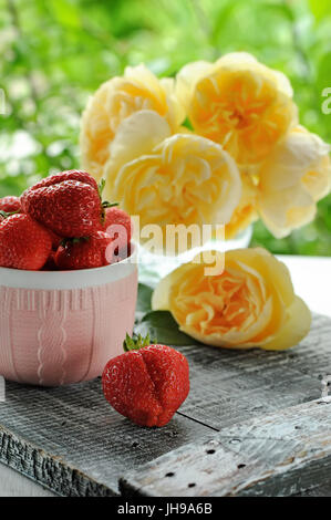 Reife Erdbeere in einer Tasse rosa Keramik auf einem Hintergrund von gelben Rosen. Die vertikalen Rahmen. Stockfoto