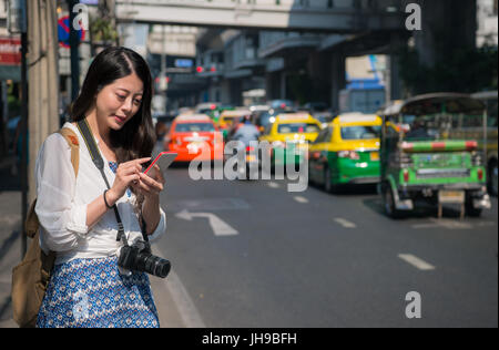 Asiatischen Backpacker Frau mit Handy-app für Car sharing-Service oder Telefon app, Richtungen und Führer während der Fahrt auf Straße in Bangk finden Stockfoto