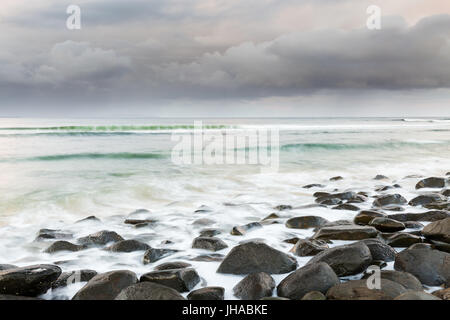 Ein Sturm geht am Horizont wie Wellen über einen Boulder übersäten Strand in dieser Szene Seelandschaft zu waschen. Stockfoto