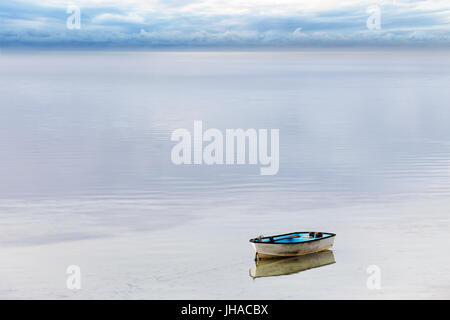 Eine kleine hölzerne Beiboot festgemacht an einer ruhigen Bucht des Wassers während ein Sturms am Horizont vorbei. Stockfoto