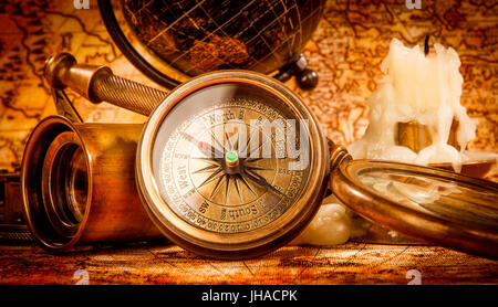 Vintage Kompass, Lupe, Taschenuhr, Federkiel, Spyglass liegen auf einer alten antiken Karte 1565 mit eine brennende Kerze. Vintage Stillleben. Stockfoto