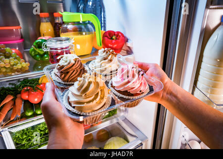 Frau nimmt den süßen Kuchen aus dem offenen Kühlschrank Stockfoto