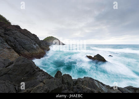 Rauh, leuchtende Blau des Ozeans umspült einer felsigen Landzunge unter Gewitterhimmel in diesem schönen Seenlandschaft. Stockfoto