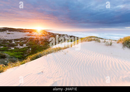 Platzt die Sonne über dem Horizont, beleuchtet die Sanddünen und die umliegende Küste in diesem schönen Seenlandschaft. Stockfoto