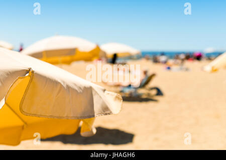 Nahaufnahme von einigen beigen Sonnenschirmen und an einem Strand im Mittelmeer, mit vielen unkenntlich Menschen Sonnenbaden im Hintergrund Stockfoto