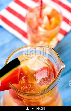 Nahaufnahme von einem Krug und ein Glas mit erfrischenden spanische Sangria Blanca, weiße Sangria mit frischen Fruchtstücken, auf einem rustikalen Holztisch blau Stockfoto