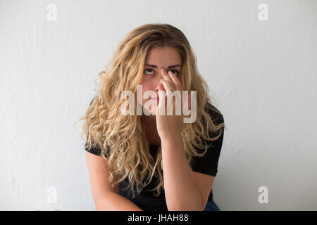 Jung, blond, Kaukasische Frau verärgert beim hinsetzen. Auf der Suche nach außerhalb des Bildschirms und nicht Blickkontakt vor einem weißen Hintergrund in natürlichem Licht. Stockfoto