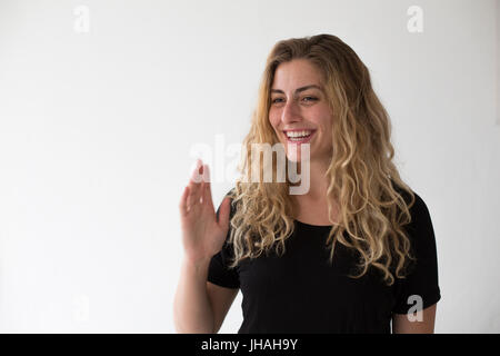 Jung, blond, schön, kaukasischen Milennial Frau zum Ausdruck bringen Aufregung und Glück während winken vor einem weißen Hintergrund. Einladend, begrüßen. Stockfoto