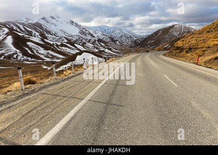 Eine kurvenreiche Alpenstraße verschwindet in der Ferne unter schneebedeckten Berge in Neuseeland. Stockfoto