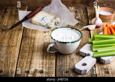 Becher blau Frischkäse Knoblauch Dip-Sauce mit Sellerie und Karotte klebt auf rustikalen Holztisch Stockfoto