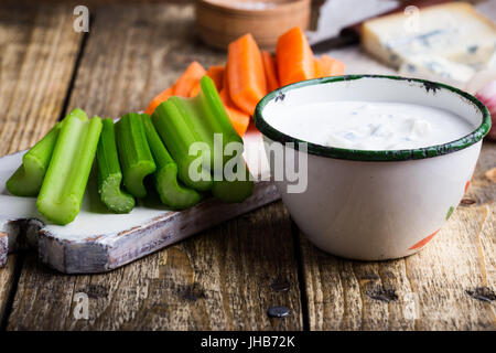 Becher blau Frischkäse Knoblauch Dip-Sauce mit Sellerie und Karotte klebt auf rustikalen Holztisch Stockfoto