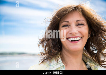 Glücklich mittlere gealterte Frau mit strubbeligem Haar am Strand lachen Stockfoto