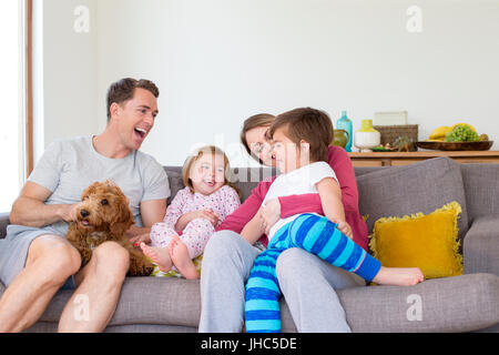 Vierköpfige Familie sitzen auf dem Sofa im Wohnzimmer ihres Hauses zusammen mit ihrem Hund. Stockfoto