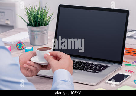 Mans Hände mit Tasse Kaffee vor offenen Laptop Modell auf Schreibtisch Stockfoto