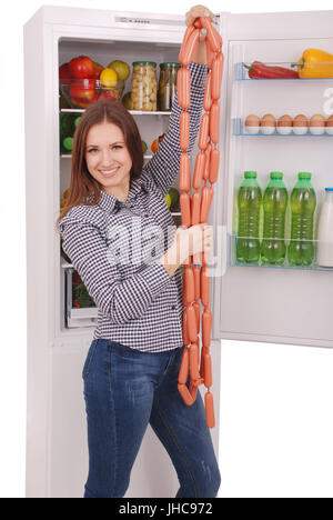 Junges Mädchen hält Würstchen auf dem Kühlschrank Hintergrund. Schöne junge Mädchen in der Nähe der Kühlschrank. Stockfoto