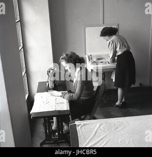 der 1950er Jahre, England, zwei Studentinnen im Haus auf einen Lehrer training College in einer Sitzung an einem kleinen Tisch mit einer Hand getrieben Singer-Nähmaschine, die andere an einem Waschbecken. Stockfoto