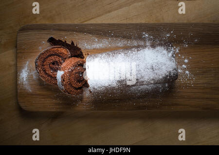 Overhead Schuss ein voller Länge Schokolade Weihnachten Yule Log oder Biskuitrolle Kuchen auf langen hölzernen Paddel Board mit weißen Puderzucker bestäubt. Stockfoto