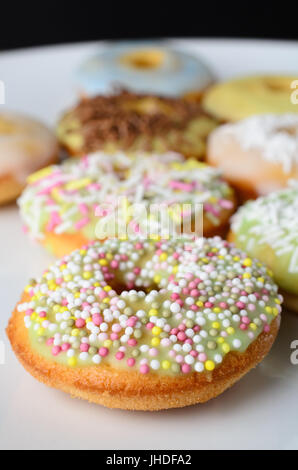 Eine Auswahl von Mini Donut geformte Kuchen auf einem weißen Teller mit einer Vielzahl von dekorativen Streuseln. Stockfoto
