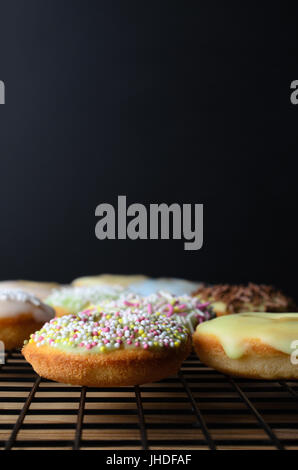 Mini Donut Kuchen verziert mit einer Vielzahl von Streusel auf einem schwarzen Draht Kühlregal mit Holztisch unter.  Schwarze Tafel Hintergrund provi Stockfoto