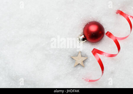 Aufwand für Weihnachten Hintergrund mit dekorative Rote Christbaumkugel, Band Wirbel und hölzernen Sterne teilweise begraben in künstlichen weißen Schnee auf der rechten Seite. Kopie Stockfoto