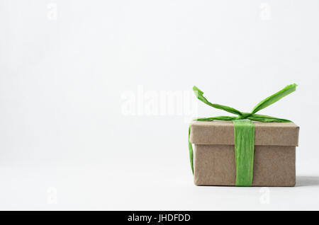 Auge Ebene Schuss von einfachen braunen Geschenk-box in der unteren rechten Ecke des Rahmens mit geschlossenem Deckel, weißer Hintergrund mit leichten grünen Bast Band auf abgebunden. Stockfoto