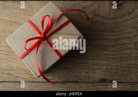 Overhead Schuss eine schlichte braune Geschenkbox mit Weihnachten Red Ribbon und eine leere Beschriftung für textfreiraum Set auf alte Eiche Holz Beplankung. Stockfoto