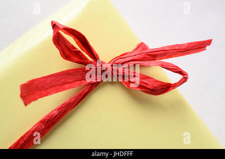 Nahaufnahme von einem gebundenen roter Bast Bogen um eine gelbe Geschenkpackung verpackt. Stockfoto