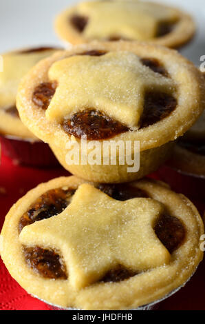 Nahaufnahme von Weihnachten Mince Pies mit Stern geformte Kuchen Spitzenwerken, gestapelt auf einem weißen Teller mit Krümel; eine rote Serviette. Stockfoto