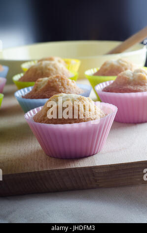 Reihen von frisch gebackenen Cupcakes in bunten Silikon Fällen.  In Reihen auf Schneidbrett aus Holz mit Misch-Schüssel und Löffel aus Holz in Zeitmessung angeordnet Stockfoto