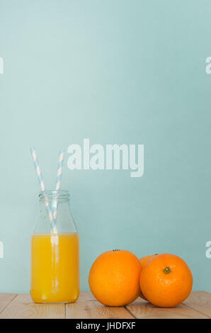 Eine Retro-Schule Milchflasche gefüllt mit frisch gepresstem Orangensaft, mit zwei blau-weiß gestreifte Strohhalme auf leichte Kiefer Holz geplankte Tisch neben grou Stockfoto