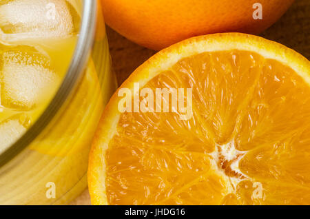 Abgewinkelt, overhead nahe Schuss frisch gepressten Orangensaft im Glas mit Eiswürfeln.  halben Orange mit Fleisch ausgesetzt und ganze ungeschälte Orange auf hölzernen ta Stockfoto