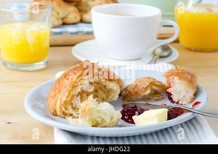 Kontinentales Frühstück gedeckten Tisch gelegt mit Croissants, Orangensaft und Kaffee. Eine Portion von teilweise gegessen Croissant mit Butter und Marmelade ist in der f Stockfoto