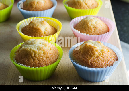 Zeilen der frisch gebackene Muffins auf Schneidbrett aus Holz in hellen, bunten Silikon Fällen. Stockfoto