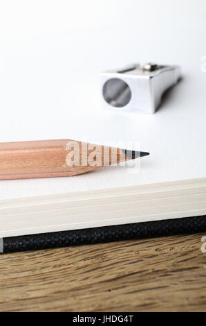 Abgewinkelt, nahe auf der Spitze einer hölzernen Graphit Zeichnung Bleistift am Rande einer leeren Skizze Buchseite mit spitzer in soft-Fokus-Hintergrund. Stockfoto