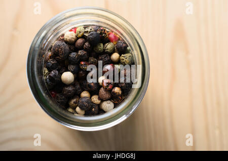 Overhead Nahaufnahme Schuss gemischte Pfefferkörner in einem Glasbehälter auf einen hellen Holztisch mit textfreiraum auf der rechten Seite. Stockfoto