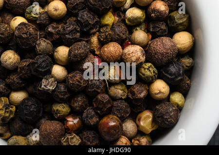 Overhead schließen bis (Makro) eine Vielzahl von gemischte Pfefferkörner, eine weiße Keramik Schüssel füllen. Stockfoto