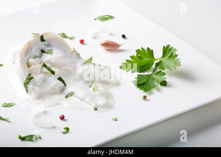 Nahaufnahme von Heringsfilets in Mayonnaise-Sauce mit Kräutern auf quadratischen Platte Stockfoto