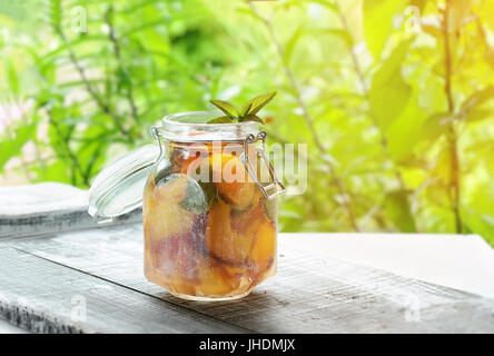 Kanne mit Deckel mit Wasser, detox mit Stücken von Pfirsich und Aprikose, mit Eis. Ein erfrischendes Getränk auf einem grünen Hintergrund. Stockfoto