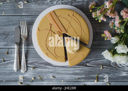 Bäckerei mit ungewöhnlich gelbe Mousse Torte mit Mandel-Dacquoise, Himbeer-Confit, knusprige Schicht mit karamellisierten Haselnüssen und Himbeere Pulver, Mousse, basierend auf Bitterschokolade serviert auf Holztisch Stockfoto